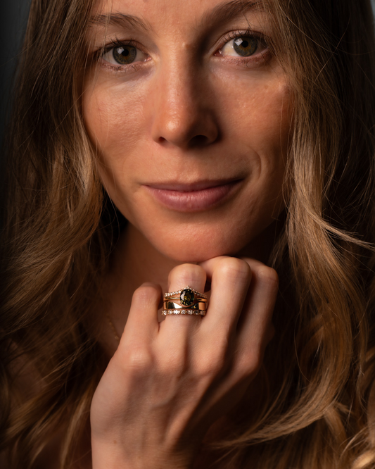 Smiling model wearing fine ring and band stack featuring diamonds and a green sapphire.